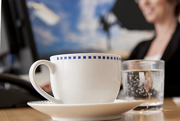 Kaffeetasse, dahinter die Hände von zwei Menschen in einer Bewerbungsberatung